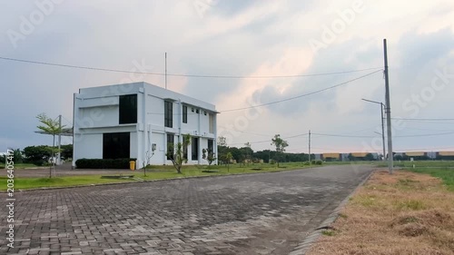 A modern white building stands beside a quiet road under a cloudy sky, creating a calm suburban atmosphere before the rain arrives.