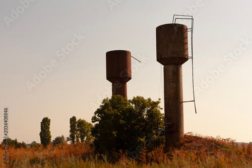 Two old concrete water towers stand tall against a hazy sky in a rural landscape