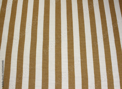 Texture of crumpled light brown and white vertical striped polyester cloth background. Close up of wrinkled classic caramel color striped fabric.
