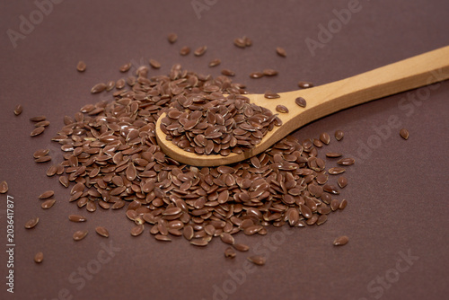 Flax seeds in a wooden spoon on brown background