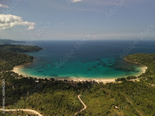 Aerial view of Batchawan Beach bay in Puerto Princesa Palawan with turquoise reef patterns sandy coastline forested hills tropical sky and open sea