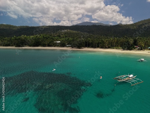 Aerial view of outrigger boats and paddleboards on turquoise water at Batchawan Beach in Puerto Princesa Palawan with sandy shore and forested hills