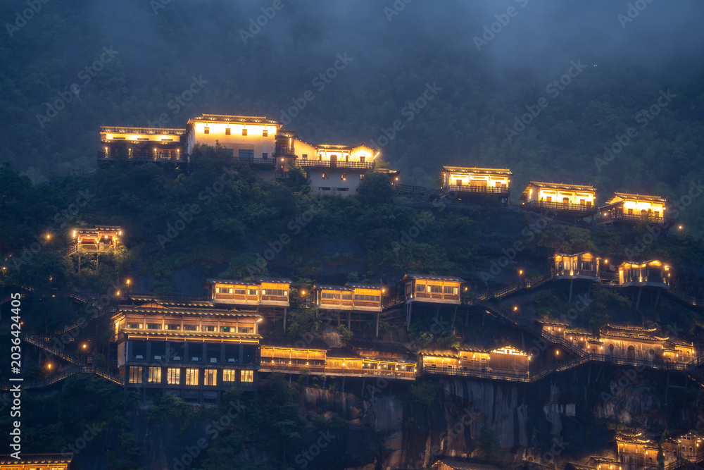 Fototapeta premium Traditional buildings with glowing lights stand on the cliffs of Wangxian Valley Scenic Area in Jiangxi China at night