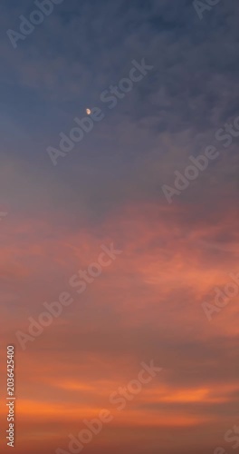 Vertical cinematic timelapse of a beautiful sunset sky with vibrant pink and orange clouds and a small moon in the center.
