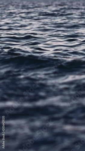 Close-up perspective of dark blue water surface with small waves and ripples reflecting subtle light. Image conveys peaceful and tranquil mood, suitable for abstract background or nature theme project