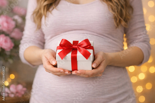 A joyous moment captured in this stock photo featuring a pregnant woman presenting a beautifully wrapped gift, perfect for any celebration or milestone.