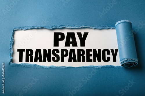 PAY TRANSPARENCY written on white paper under a torn blue edge