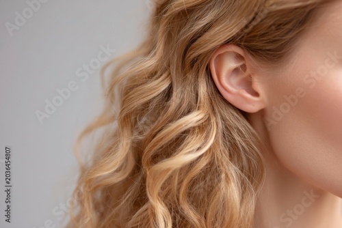 closeup of an ear with blonde, curly hair.
