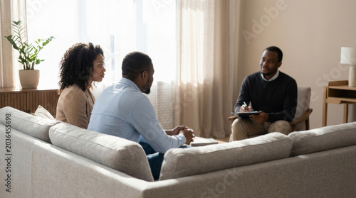 African american couple sitting on sofa talking to professional therapist. Young husband and woman at session with psychologist. Mental health support and counseling for married partner.