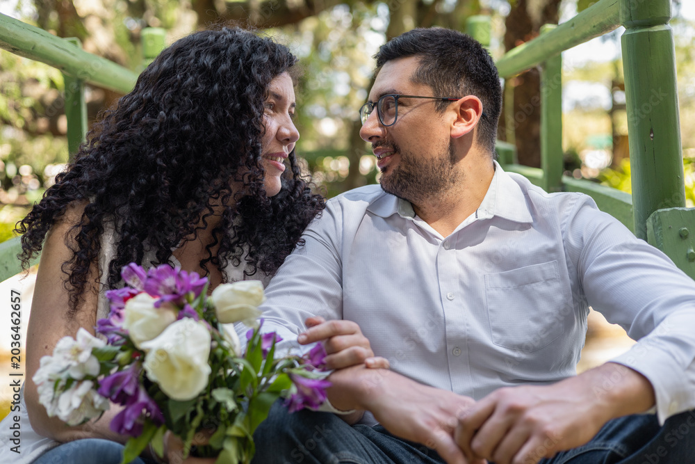 Fototapeta premium Happy couple sitting together in a garden holding a flower bouquet and sharing a warm romantic moment outdoors.