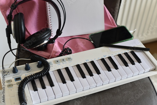 Billede på lærred White MIDI keyboard with headphones and smartphone on pink fabric