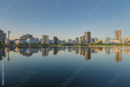Wide panoramic skyline around Cau Giay Lake mirrored across still water under clear evening light in Hanoi.