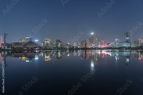 Night skyline of Cau Giay Lake features illuminated buildings and colorful reflections across calm urban waters in Hanoi.