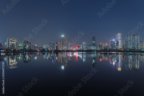 Illuminated bridge and modern skyline reflect across tranquil Cau Giay Lake during a peaceful Hanoi night scene.