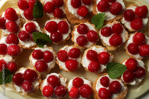 Konstfotografi Top-down view of mini raspberry tartlets with creamy white filling and fresh mint leaf garnish, featuring a vibrant and elegant dessert arrangement