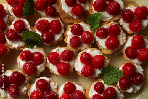 Obraz na płótnie Fresh raspberry tartlets with creamy white filling and mint leaf garnishes, captured in a flat lay composition with vibrant red and green tones