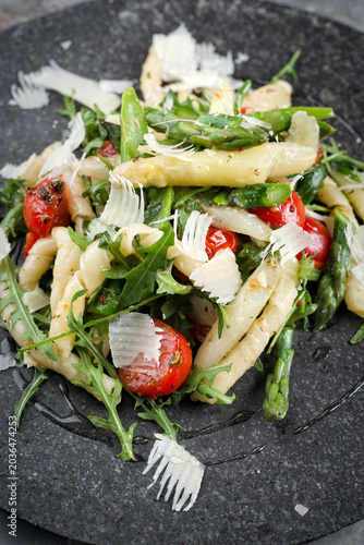 Cold vegetarian pasta noodle salad with green and white asparagus tips, arugula, fresh tomatos and parmesan served as close-up on a black stone plate