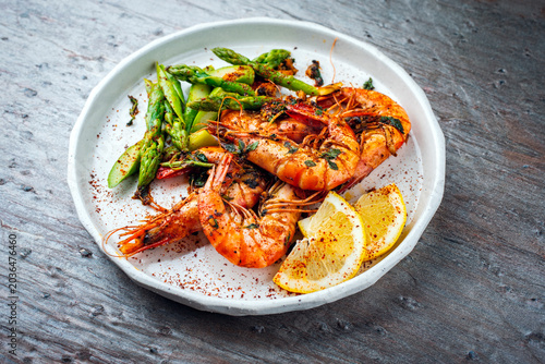 Grilled spicy white tiger prawns in shell with green asparagus served as tapas as close-up on a design plate