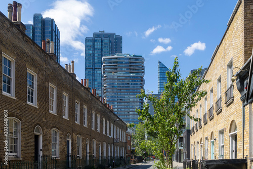 London, UK, Roupell Street, a historic street with brick terraced houses, contrasted by modern skyscrapers in the background, including the nearby Canaletto residential tower on City Road.