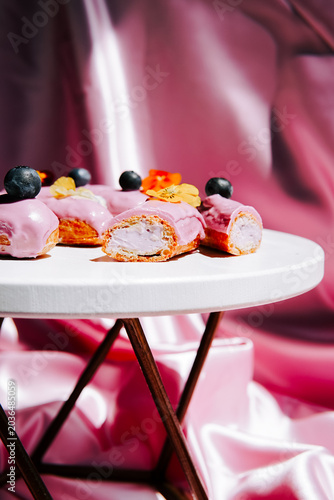 Sweet pink eclairs adorned with fresh blueberries and delicate flowers on white table