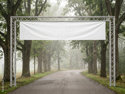 Large white event banner mockup on metal truss over forest road