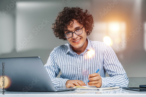 Slika na platnu A young adult working with a laptop and notes in a realistic style on a bright o