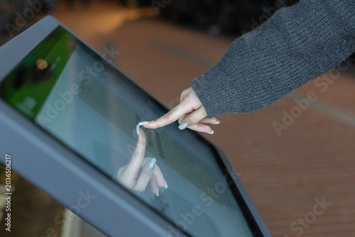 Interactive digital kiosk with public transport Info, woman touching with finger interactive futuristic screen. Advanced technology