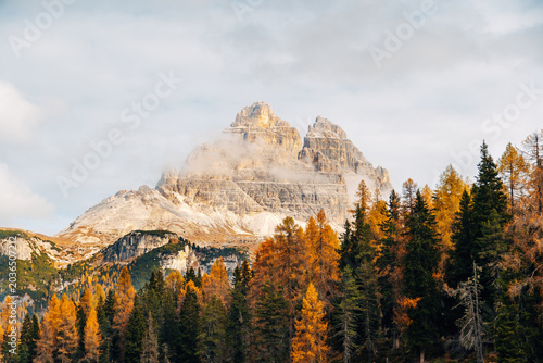 Majestic Dolomite Mountain Peak Looming Over Vibrant Autumn Forest, Dramatic Alpine Landscape in Golden Fall Colors