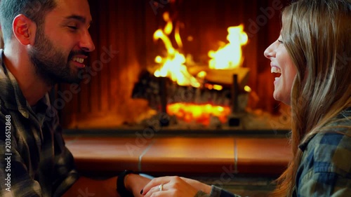 Romantic couple holding hands by fireplace. Young couple enjoying a romantic moment holding hands and talking in front of a cozy fireplace