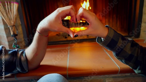 Romantic couple making heart shape with hands. Young happy couple making a heart shape with their hands in front of a cozy fireplace at home