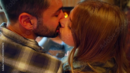 Romantic couple kissing and relaxing by a fireplace at home. Young man and woman in love kissing by the fire, enjoying a cozy and warm winter evening together