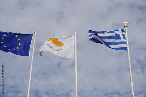 Fotografie The Cyprus, Greece, and EU flags are flying and waving in the wind in front of a cloudy sky as a symbol of freedom and European unity