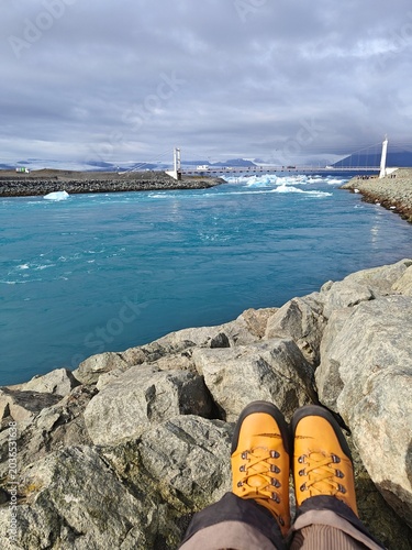 POV of traveler in yellow hiking boots looking at floating icebergs in Jökulsárlón glacial lagoon, Iceland. Adventure, freedom and Nordic nature exploration concept.