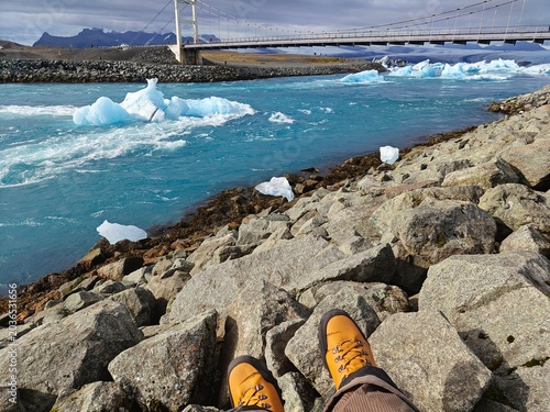 POV of traveler in yellow hiking boots looking at floating icebergs in Jökulsárlón glacial lagoon, Iceland. Adventure, freedom and Nordic nature exploration concept.