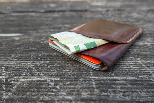 Currency in banknotes peeking out in leather wallet on wide wood wooden background