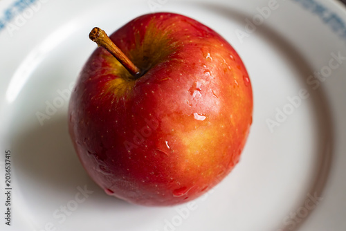 Fresh red apple with water drops on a white plate