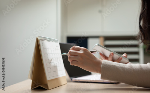 Businesswoman managing schedule and business planning with calendar and smartphone, representing task organization, appointment management, workflow planning, and productivity strategy.