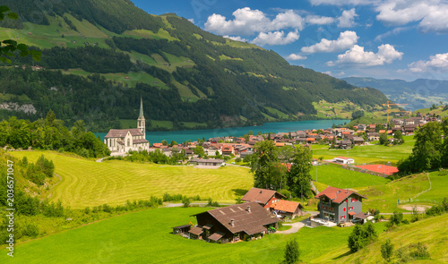 Traditional Swiss village with church buildings located near turquoise Lungern lake and green alpine slopes.
