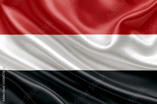 The flag of Yemen is shown with red, white, and black horizontal stripes. The fabric has a smooth texture and appears to be waving gently. The colors represent the nation.