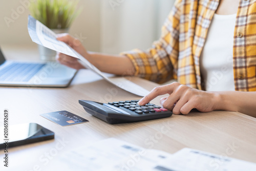 Bill pay. Online internet banking asian young woman hand using calculator for calculate expense to pay credit card, holding invoice paper for checking on table at home, make payment on laptop computer