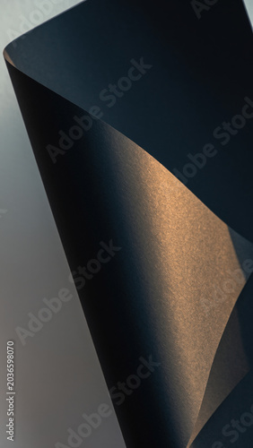 Abstract composition featuring dark, curved paper surfaces illuminated by warm, directional light creating dramatic shadows and texture contrast.