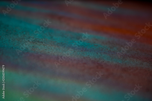 Abstract image with bands of color in reddish and turquoise tones, with a selective focus that highlights the iridescent and psychedelic texture.