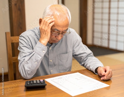 老後の経済不安：自宅の机で家計簿と通帳、電卓を前にして頭を抱え苦悩するシニア男性の姿