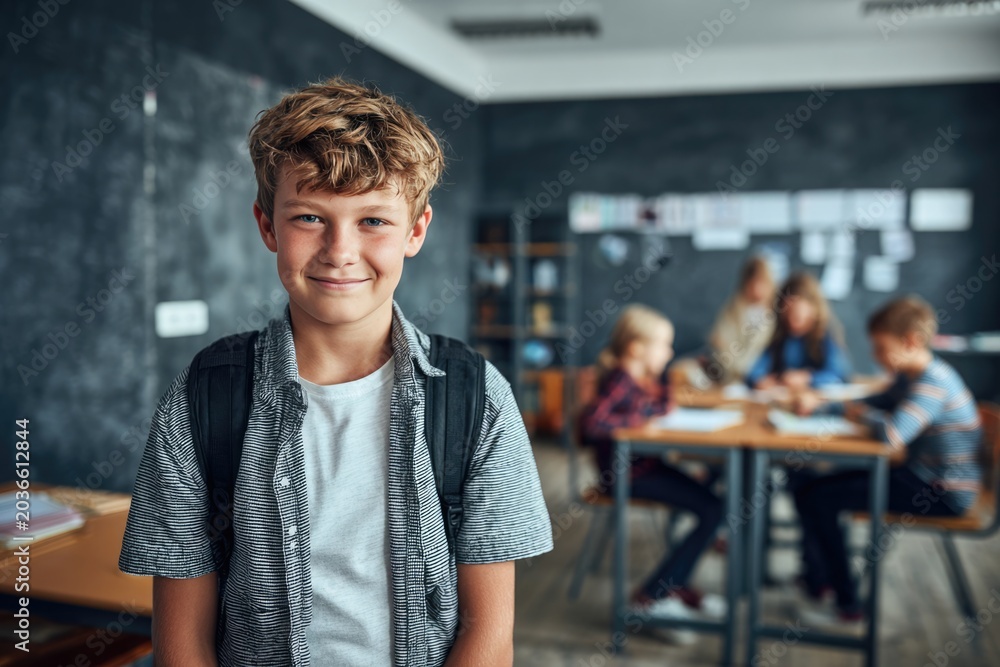 Obraz premium Young smiling student standing in classroom with backpack