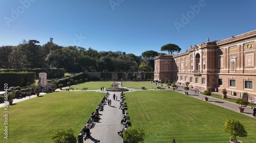 A high angle timelapse video showing crowds of tourists walking through a beautiful green garden next to an ancient historical palace architecture in Rome, Italy.
