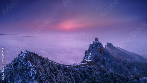 A stunning view of the Simatai Great Wall covered in snow with mist and morning light during sunrise. A breathtaking winter scene in Beijing, China.