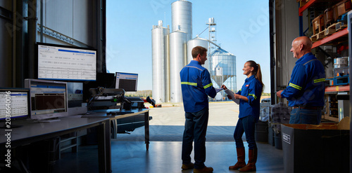 Industrial plant workers reviewing data on tablets in front of massive storage silos during a productive workday with industrial logistics business technology collaboration engineering