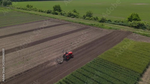 Agricultural red small tractor in the field plowing, works in the field. Flying over a tractor working in the field.