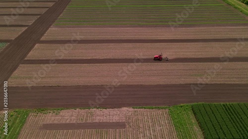 Agricultural red small tractor in the field plowing, works in the field. Flying over a tractor working in the field.