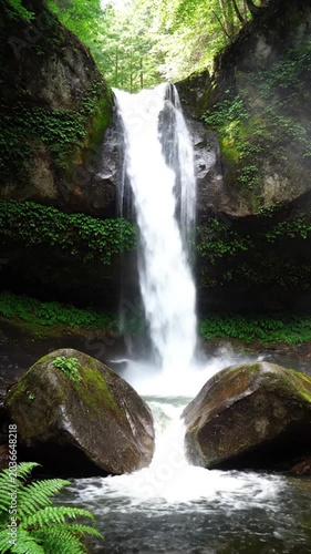 Waterfall cascading down rocky slope surrounded by lush greenery.